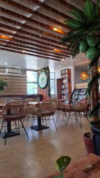 A stylish cafe interior featuring wooden elements, greenery, and rattan chairs, creating a cozy atmosphere.