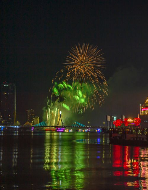 Free Colorful fireworks illuminate the night sky over a vibrant cityscape reflected in the river. Stock Photo