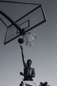 Athlete reaching for the hoop in an energetic outdoor basketball game, captured in striking black and white.