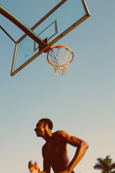 Silhouette of a basketball player in motion against an outdoor hoop during sunset.