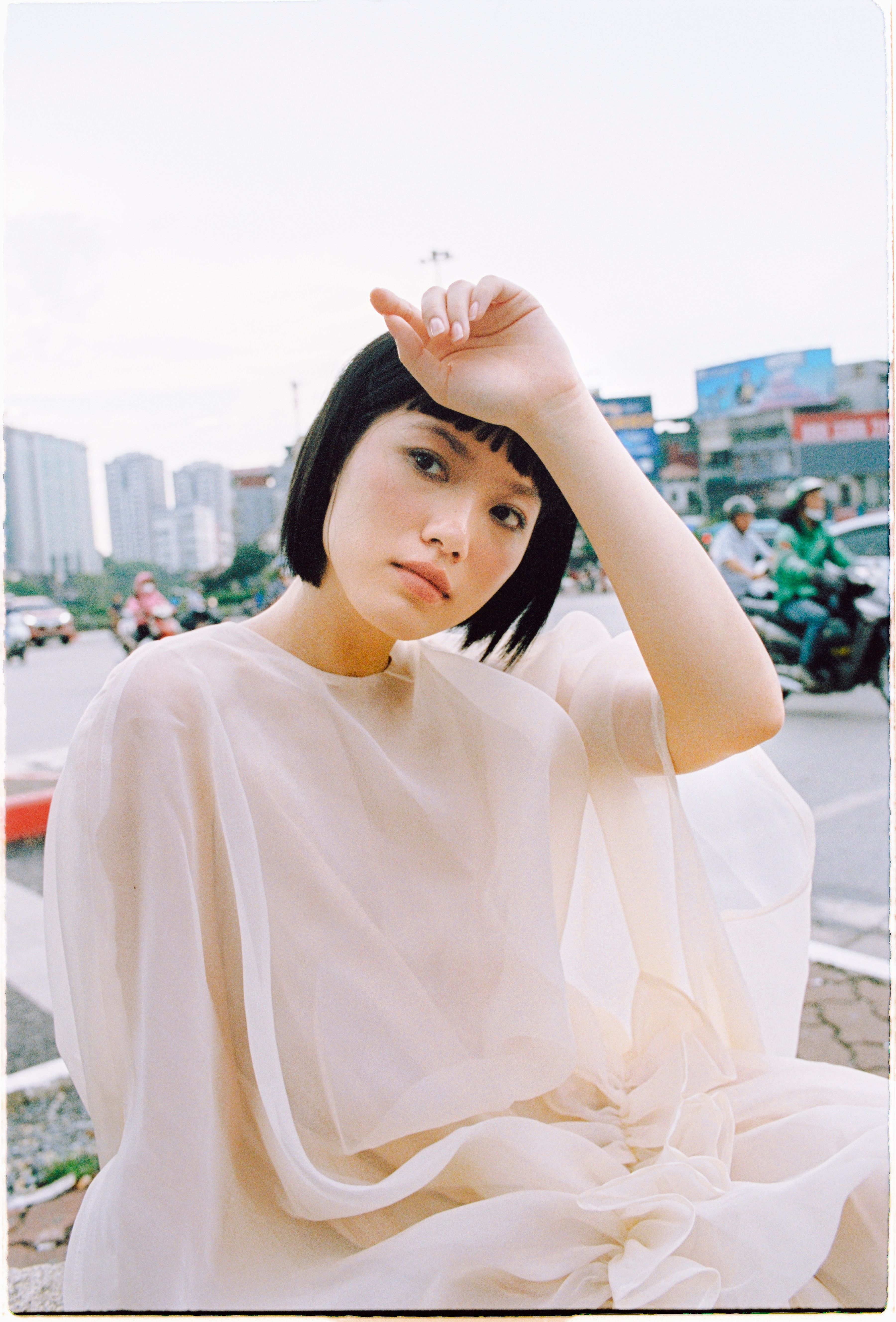 Fashionable young woman in sheer dress seated outdoors on a sunny day.