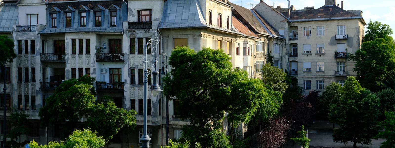 Charming view of historic European apartment buildings surrounded by lush greenery in warm afternoon light.