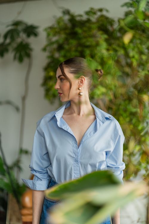 Free Stylish woman in blue shirt posing indoors surrounded by lush green plants, exuding elegance and grace. Stock Photo