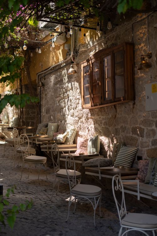 Free Cozy outdoor café with rustic stone walls and vintage seating on a sunny day. Stock Photo