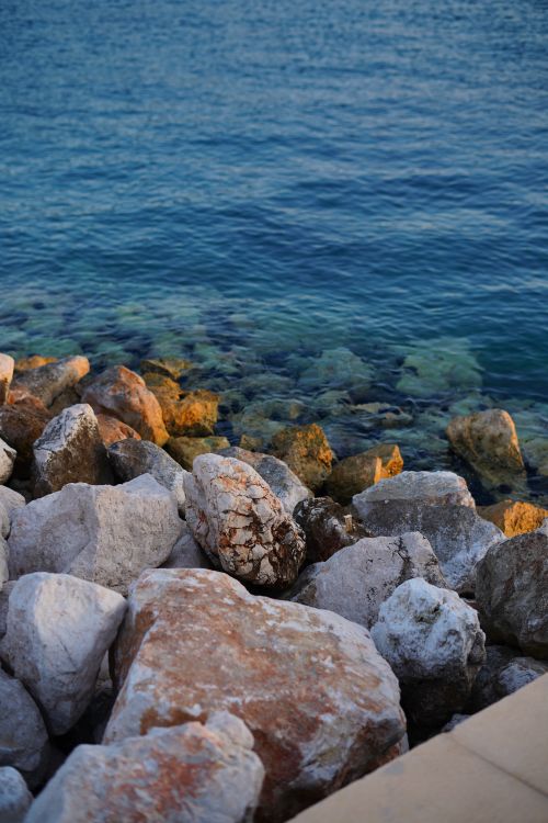 Free A serene rocky shoreline with crystal clear blue water, creating a peaceful coastal scene. Stock Photo