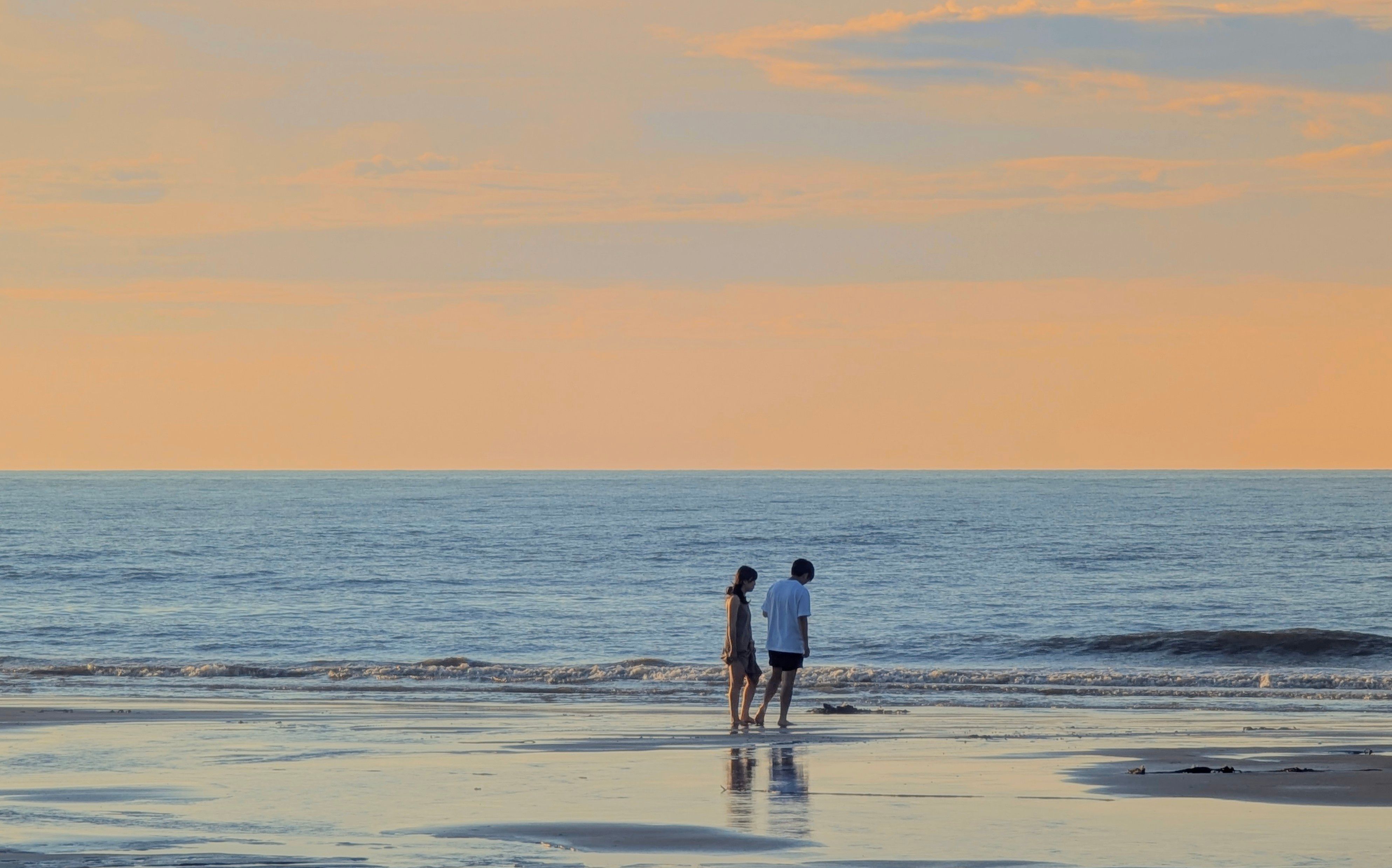 Two people walking together along the shoreline in the soft light of late afternoon
