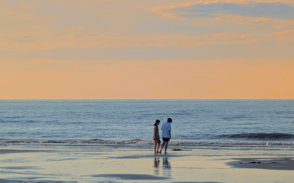 Two people walking together along the shoreline in the soft light of late afternoon
