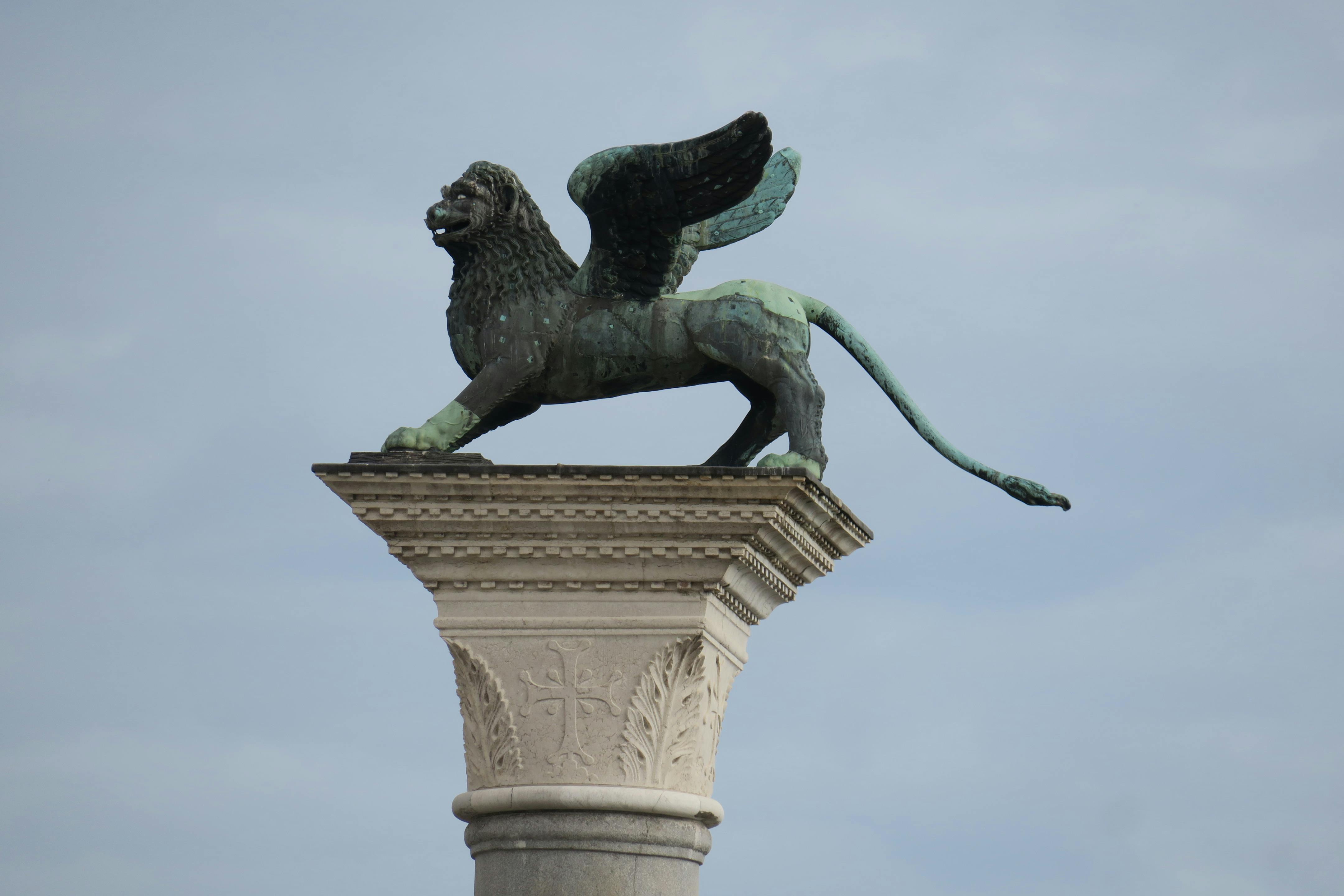 Iconic winged lion statue atop a column in Venice, Italy, against a cloudy sky.