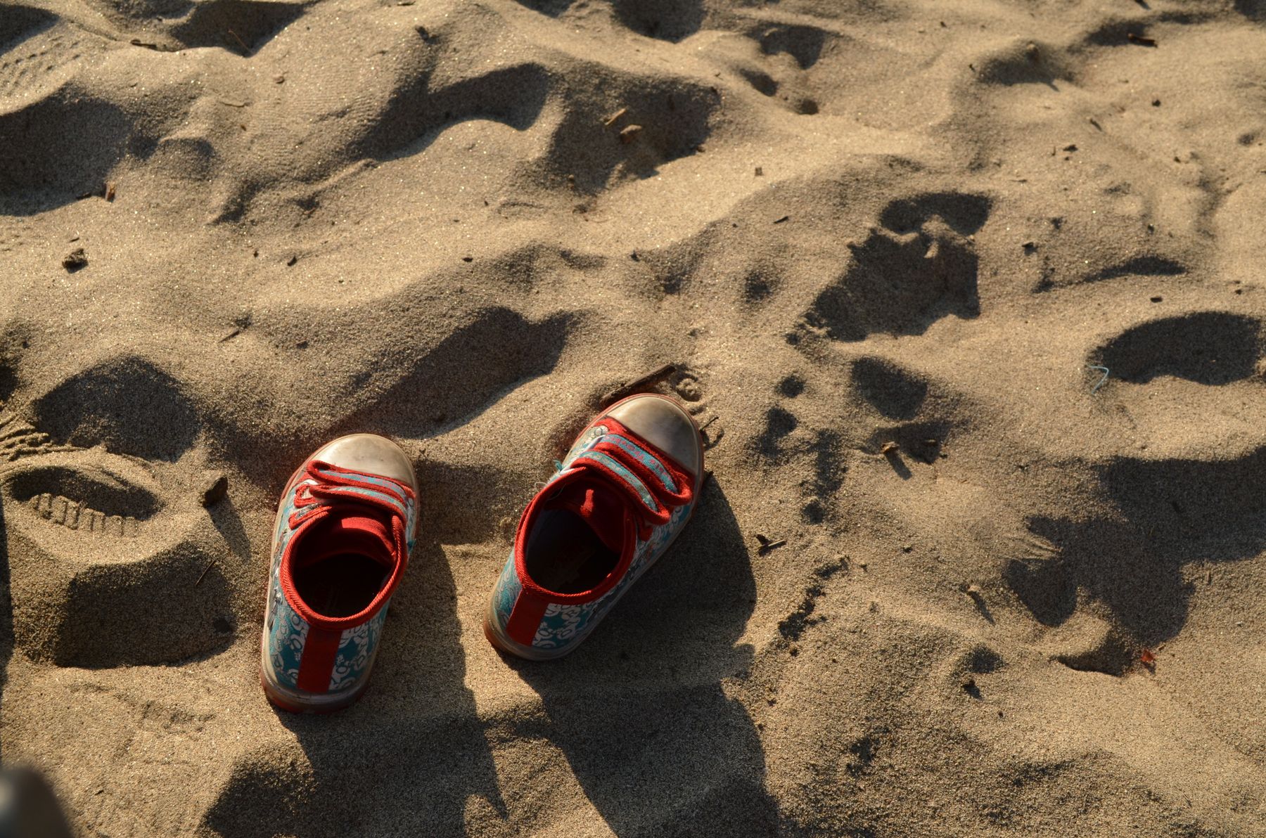 Pair of children's sneakers resting on sandy beach after outdoor play