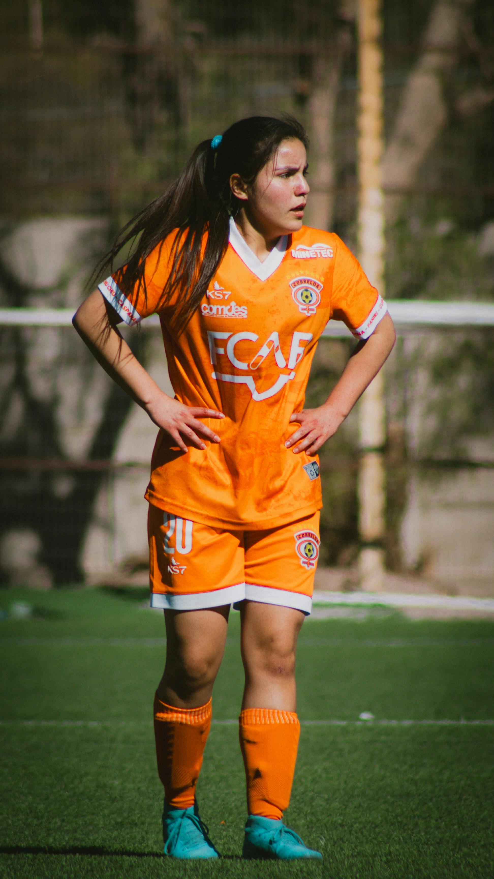 Young female football player on the field in Santiago, Chile wearing an orange team jersey during a match.