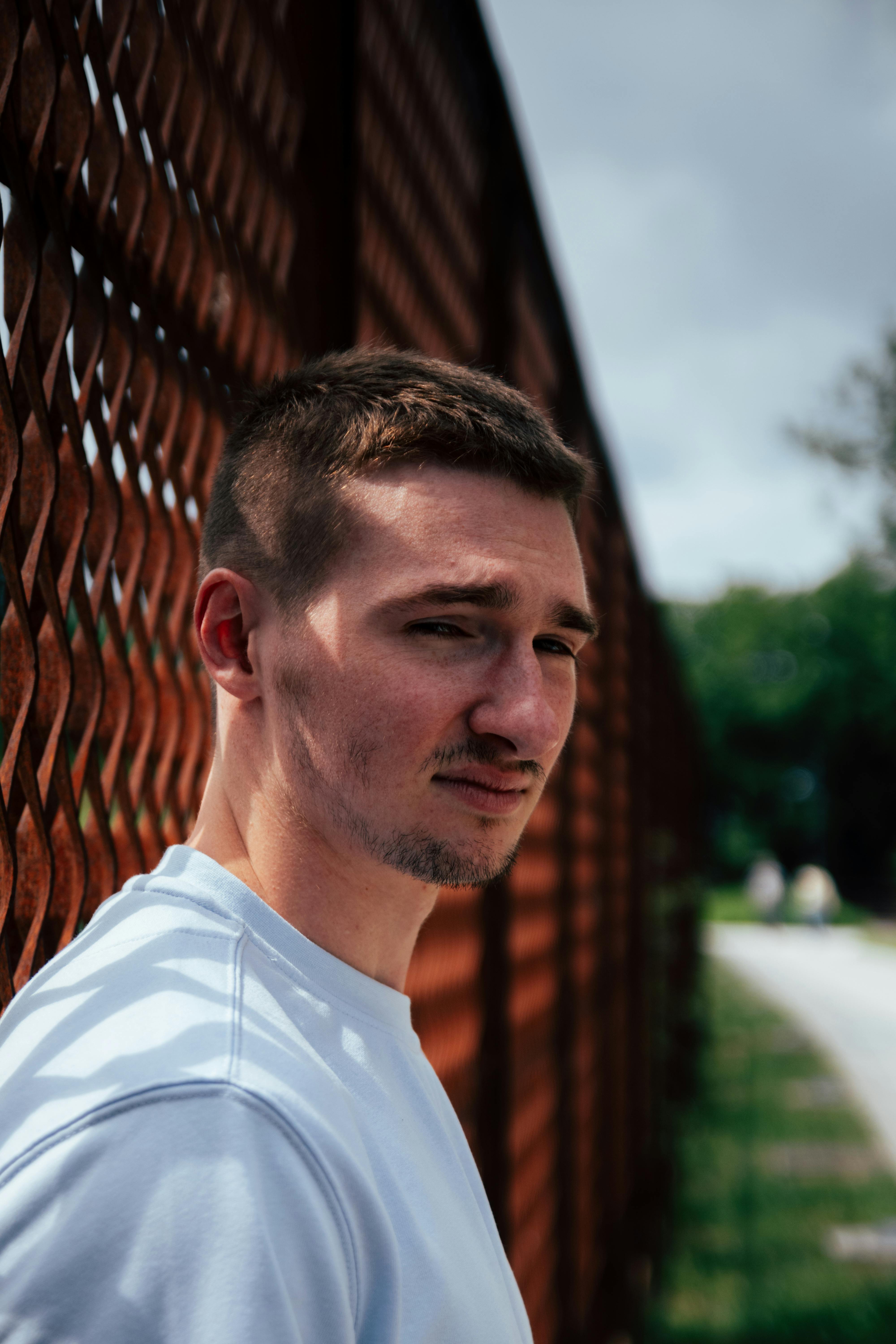 Portrait of a young man in Arras, France, standing by a red metal fence.