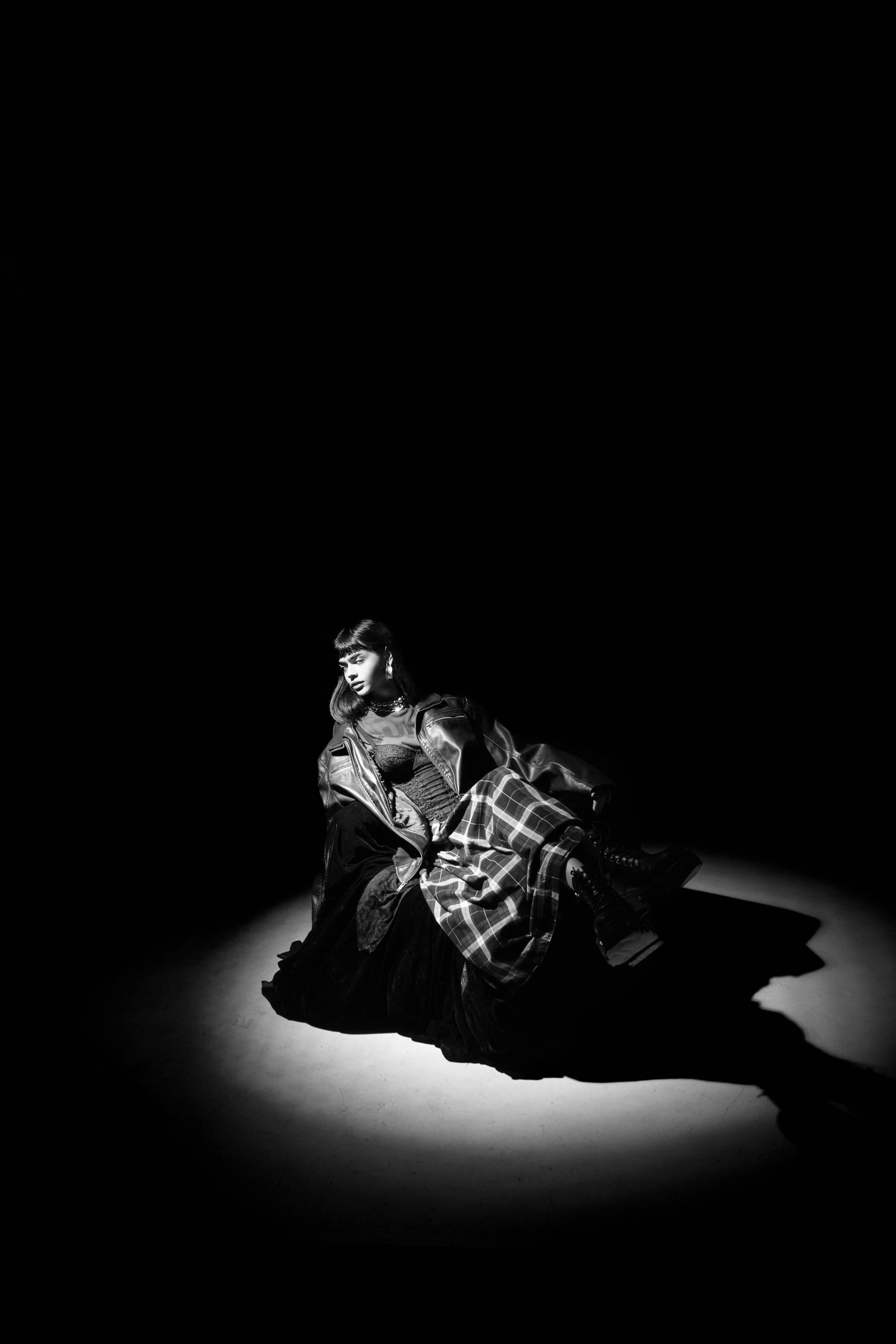 Dramatic black and white portrait of a woman in elegant attire under spotlight.