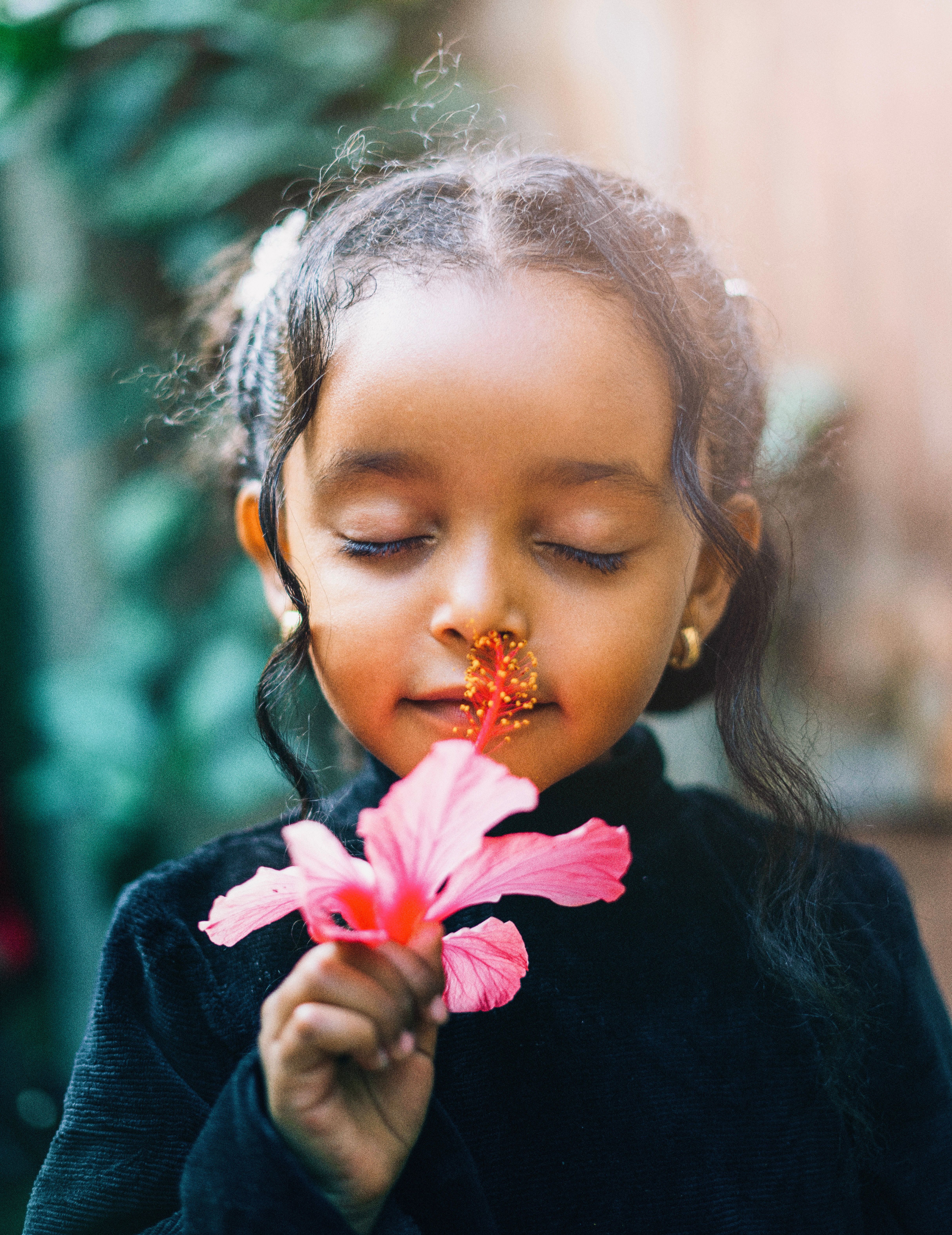 A beautiful Ethiopian child with closed eyes savoring the scent of a hibiscus flower.