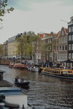 Lively Amsterdam canal with colorful boats and historic Dutch houses under a bright sky.