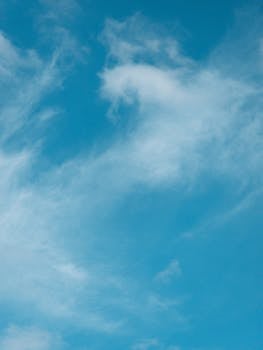 A tranquil view of a clear blue sky with soft, wispy white clouds.
