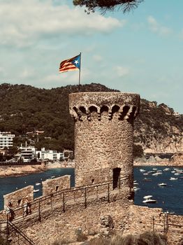 Historic stone tower with Catalonia flag on scenic Mediterranean coast of Spain.