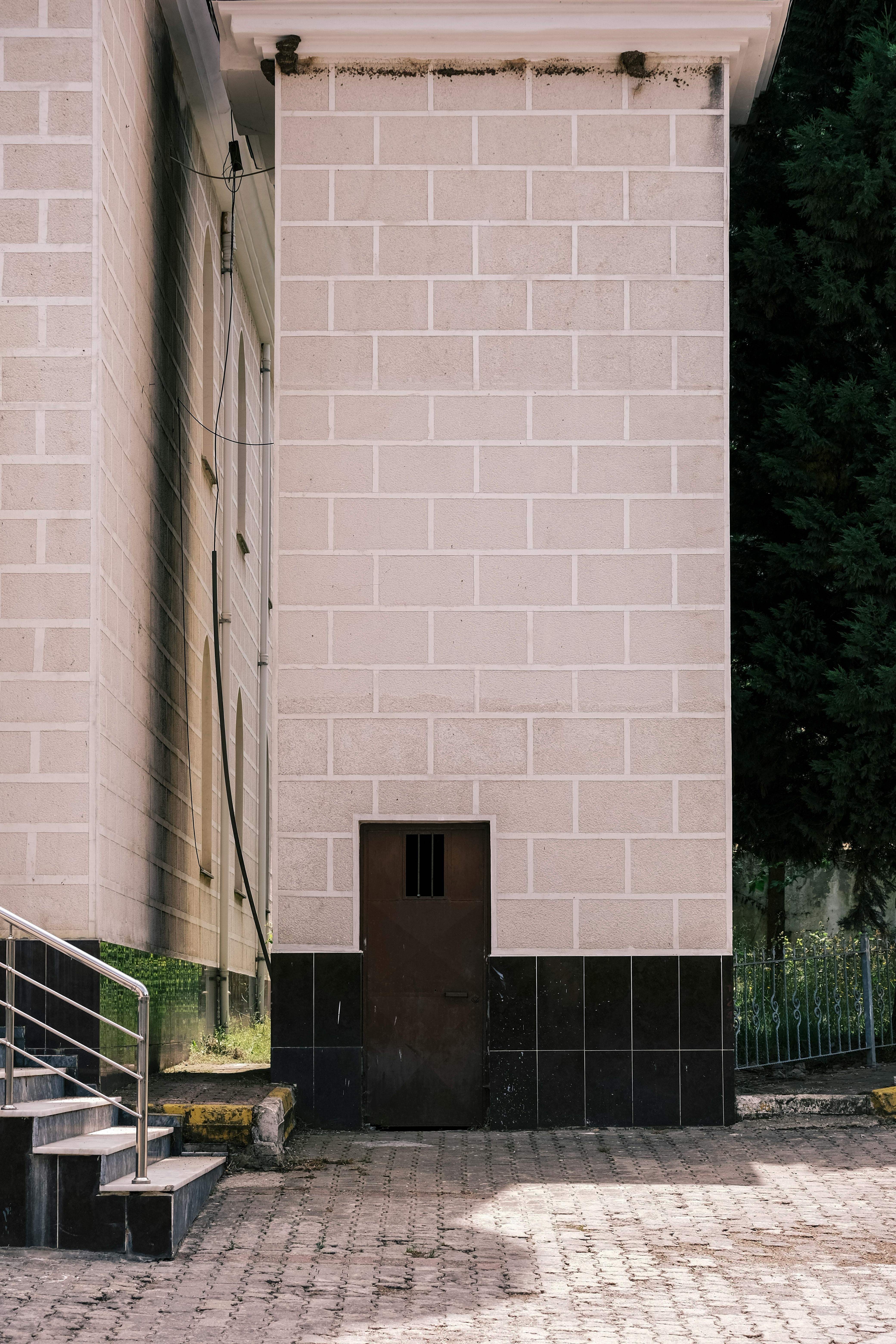 gratis Een minimalistische stedelijke scène met een hoge gebouwmuur met een kleine, donkere deur aan de onderkant. Stockfoto