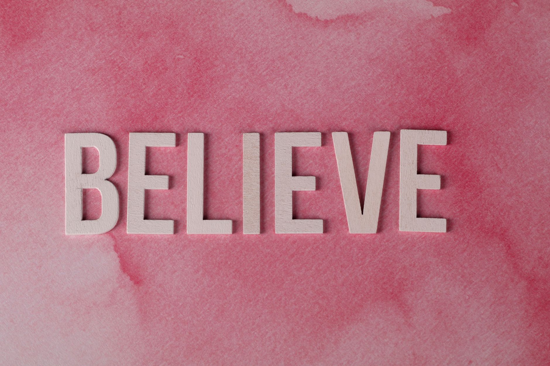 Inspirational word 'Believe' crafted on a textured pink watercolor background. Ideal for motivation.