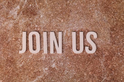 Wooden letters spelling 'Join Us' on a brown textured surface, suitable for invitations.