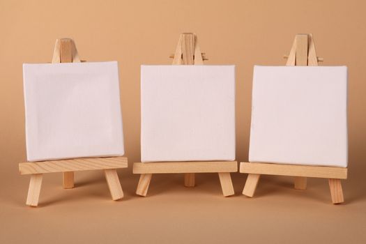 Minimalist arrangement of three blank canvases on wooden easels against a neutral background.