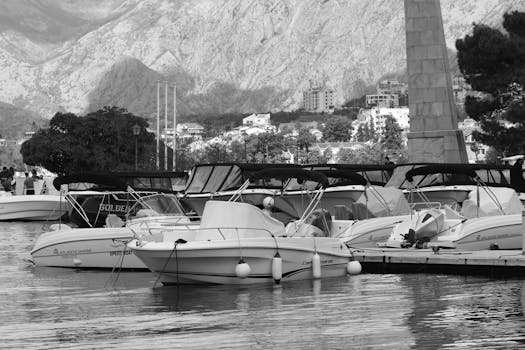 Black and white view of a marina with boats in Kotor, Montenegro, backed by mountains.