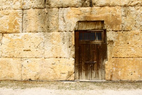 Free A rustic wooden door set in a large weathered stone wall, evoking historical architecture. Stock Photo