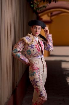 Person wearing a colorful, embroidered traditional outfit posing against a wooden wall.