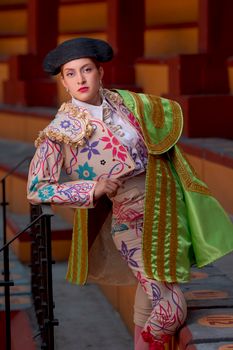 A female matador poses confidently in colorful traditional attire at a bullring.