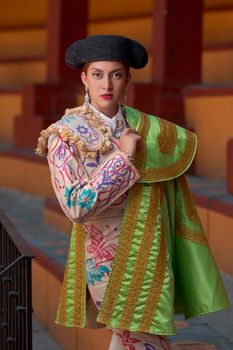 A confident female bullfighter poses in traditional attire, showcasing vibrant colors and intricate embroidery.
