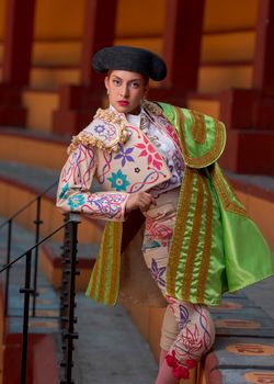 Female bullfighter dressed in a vibrant, traditional suit at a bullring, showcasing cultural attire.