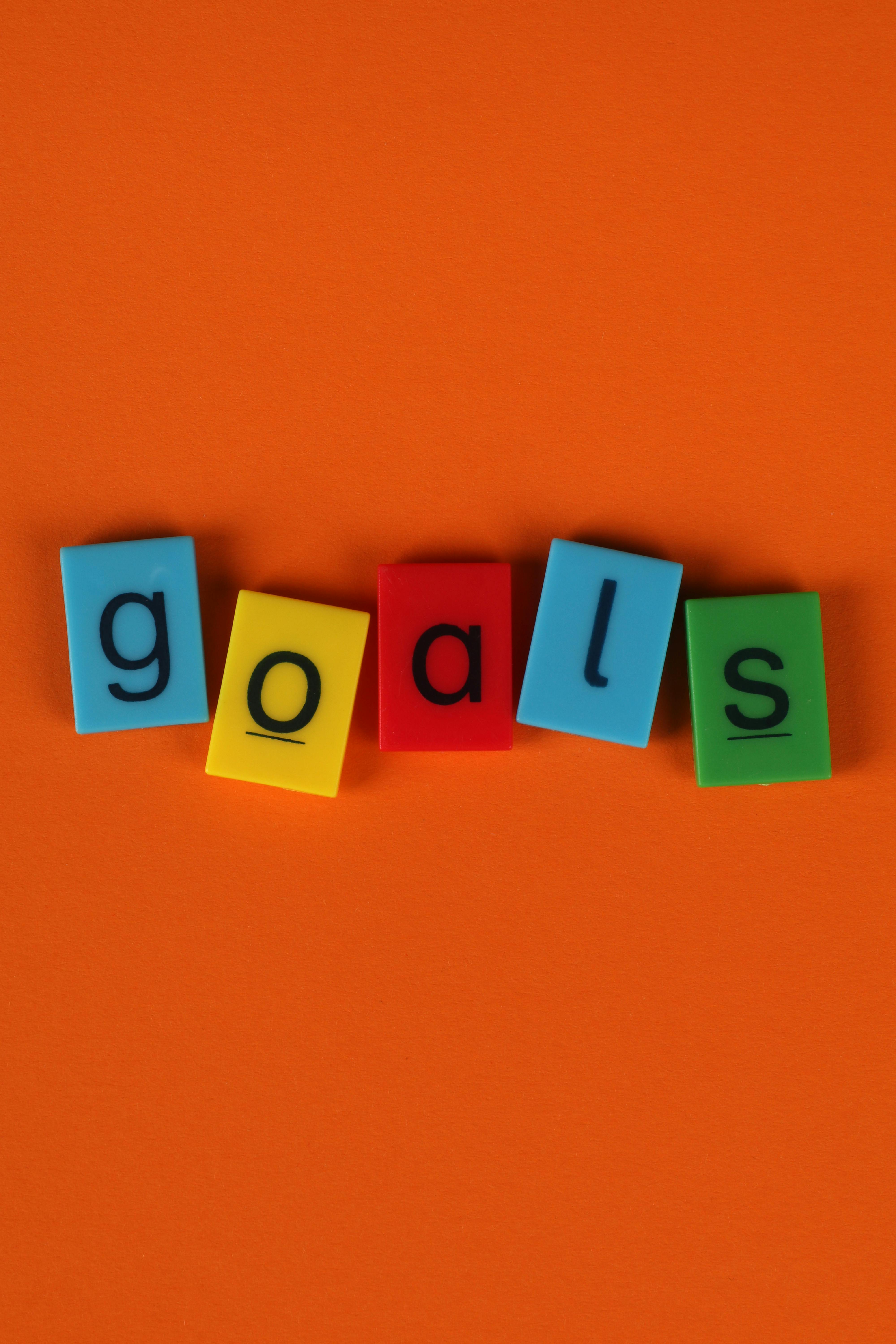 Vibrant blocks spelling 'goals' on an orange surface symbolize ambition and motivation.
