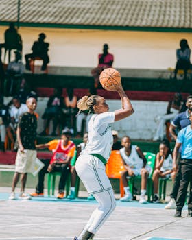 Dynamic action shot of a female basketball player shooting during a game, with spectators in the background.