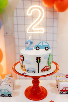 A vibrant car-themed birthday cake with number two candle, perfect for a two-year-old's celebration.