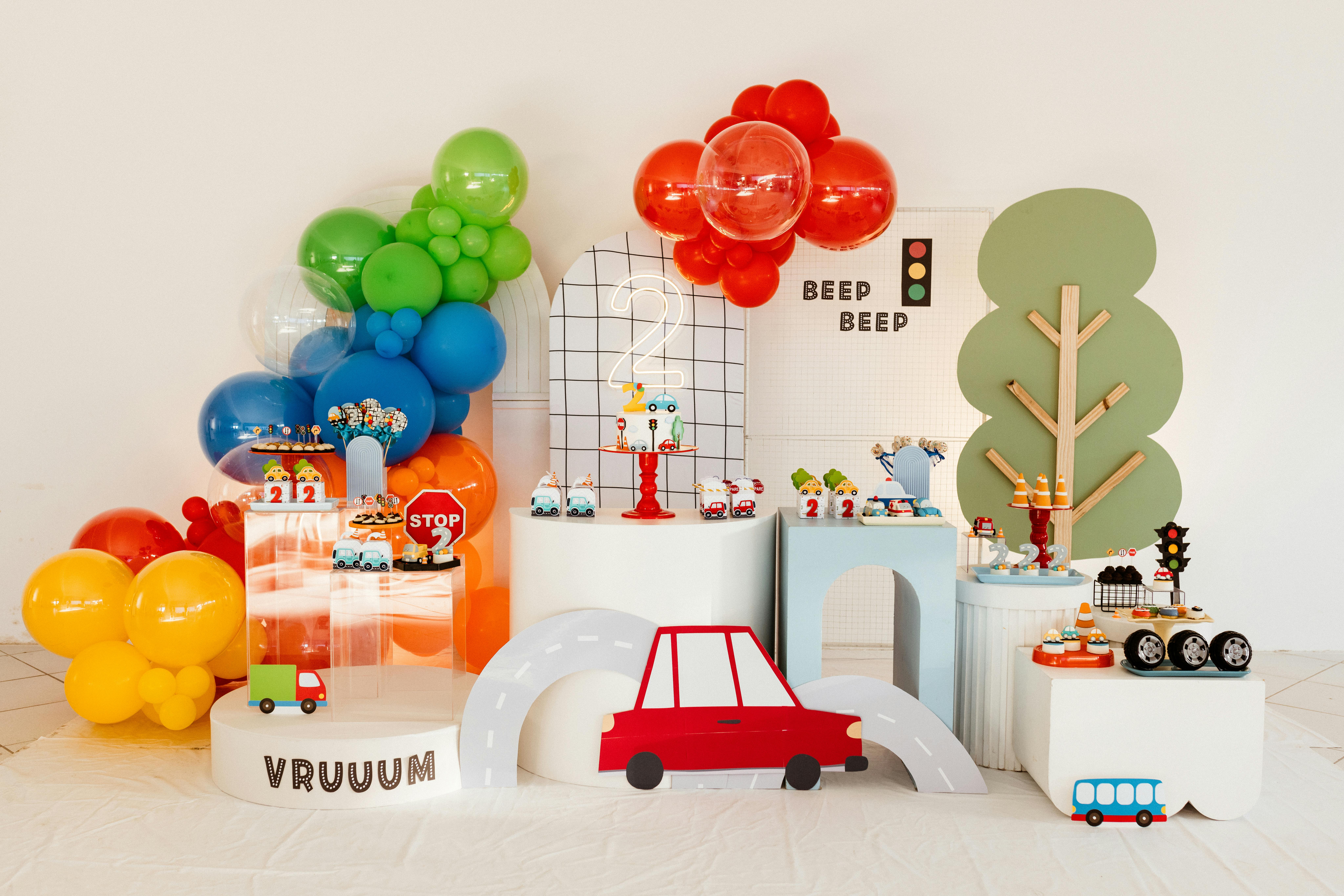 Vibrant cartoon-themed decoration setup for a child's birthday party with balloons and toy cars.