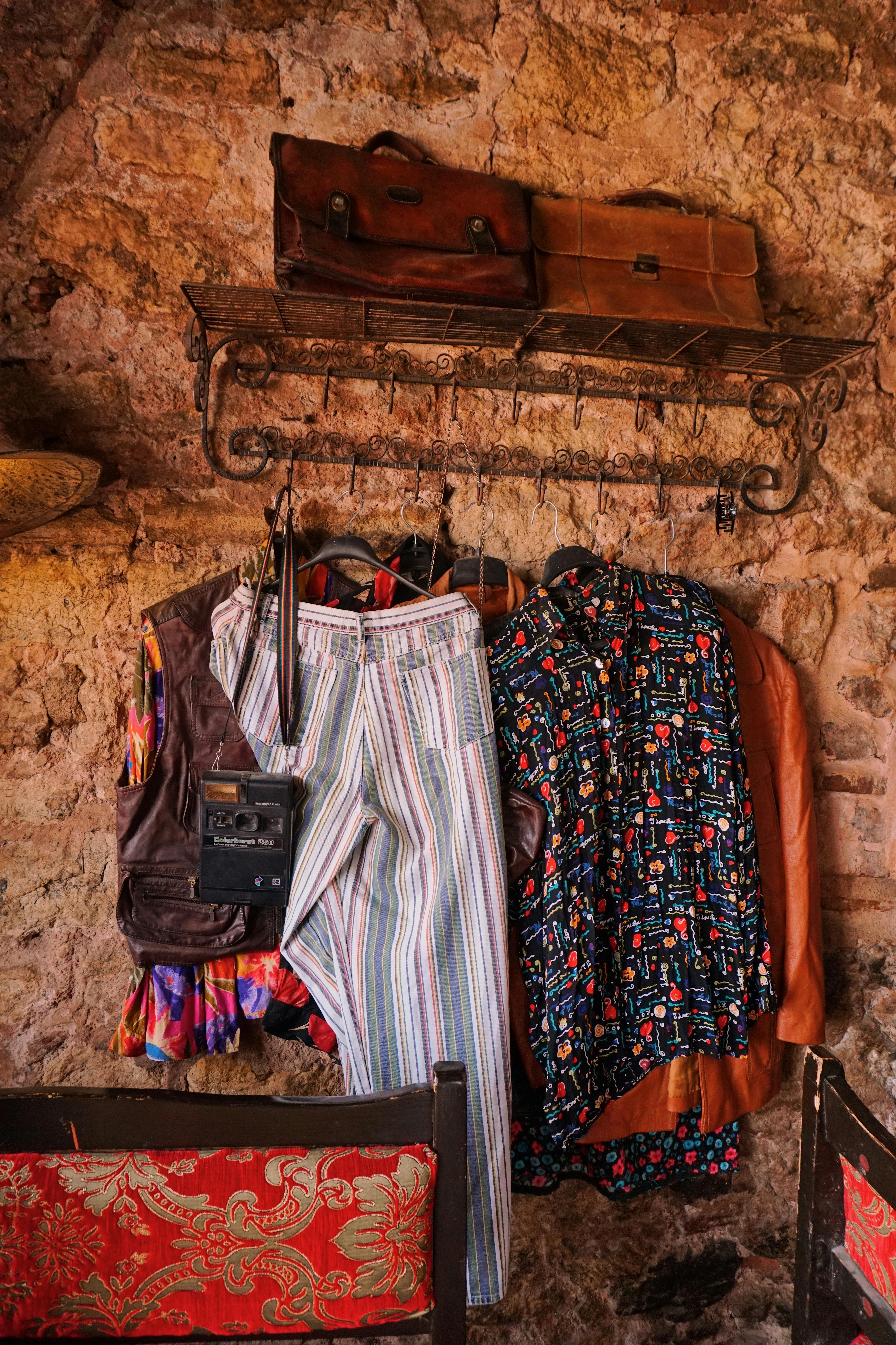 Gratuit O expunere fermecătoare de haine și accesorii vintage pe un perete rustic din piatră, evocând nostalgie. Fotografie de stoc