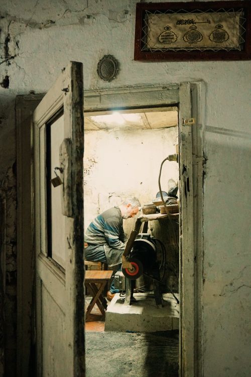 Free An elderly man works diligently in a vintage workshop, captured through an open door. Stock Photo