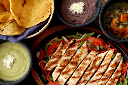 Free Delicious Mexican grilled chicken fajitas with side dishes of beans, guacamole, and tortillas. Stock Photo
