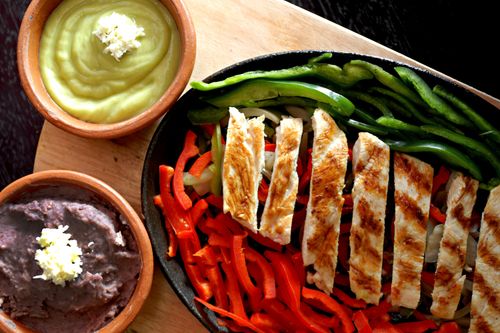 Free Sizzling grilled chicken fajitas with bell peppers, guacamole, and refried beans on a wooden board. Stock Photo