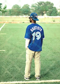 A man in a Bautista jersey stands on a sports field, facing away.
