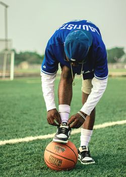 A basketball player ties shoelaces outdoors on a grass field, emphasizing preparation.