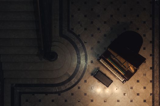 Captivating aerial view of a grand piano beside an elegant spiral staircase in subdued lighting.