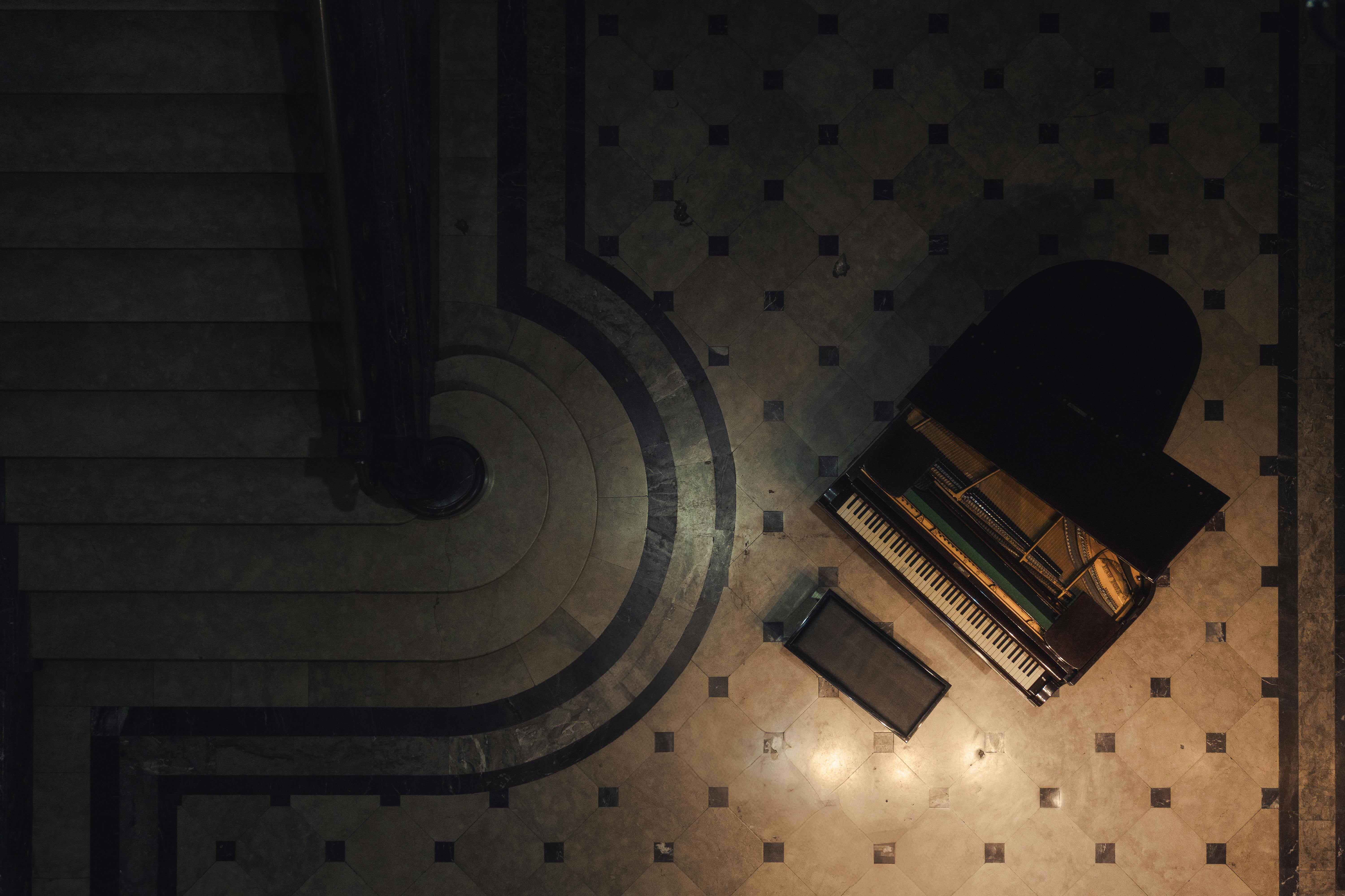 Free Captivating aerial view of a grand piano beside an elegant spiral staircase in subdued lighting. Stock Photo