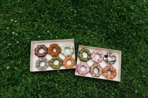 Free Boxes of decorative ring-shaped donuts placed on lush green grass, offering a colorful selection. Stock Photo