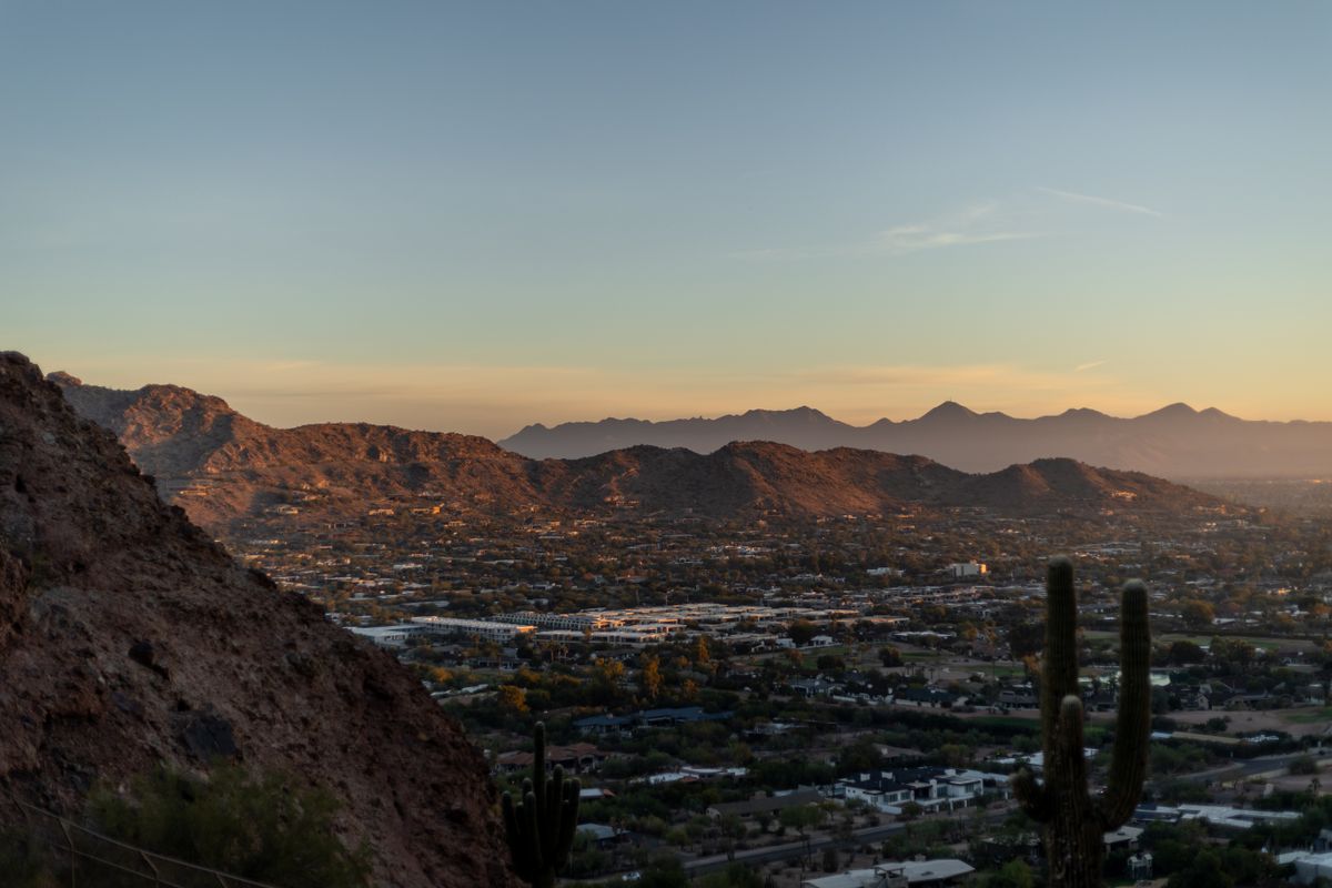 Breathtaking view of Phoenix cityscape and desert mountains at sunset with silhouetted cacti. Illustrative editorial photograph.