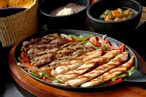 Free Sizzling platter of chicken and beef fajitas with colorful peppers served with Mexican sides. Stock Photo