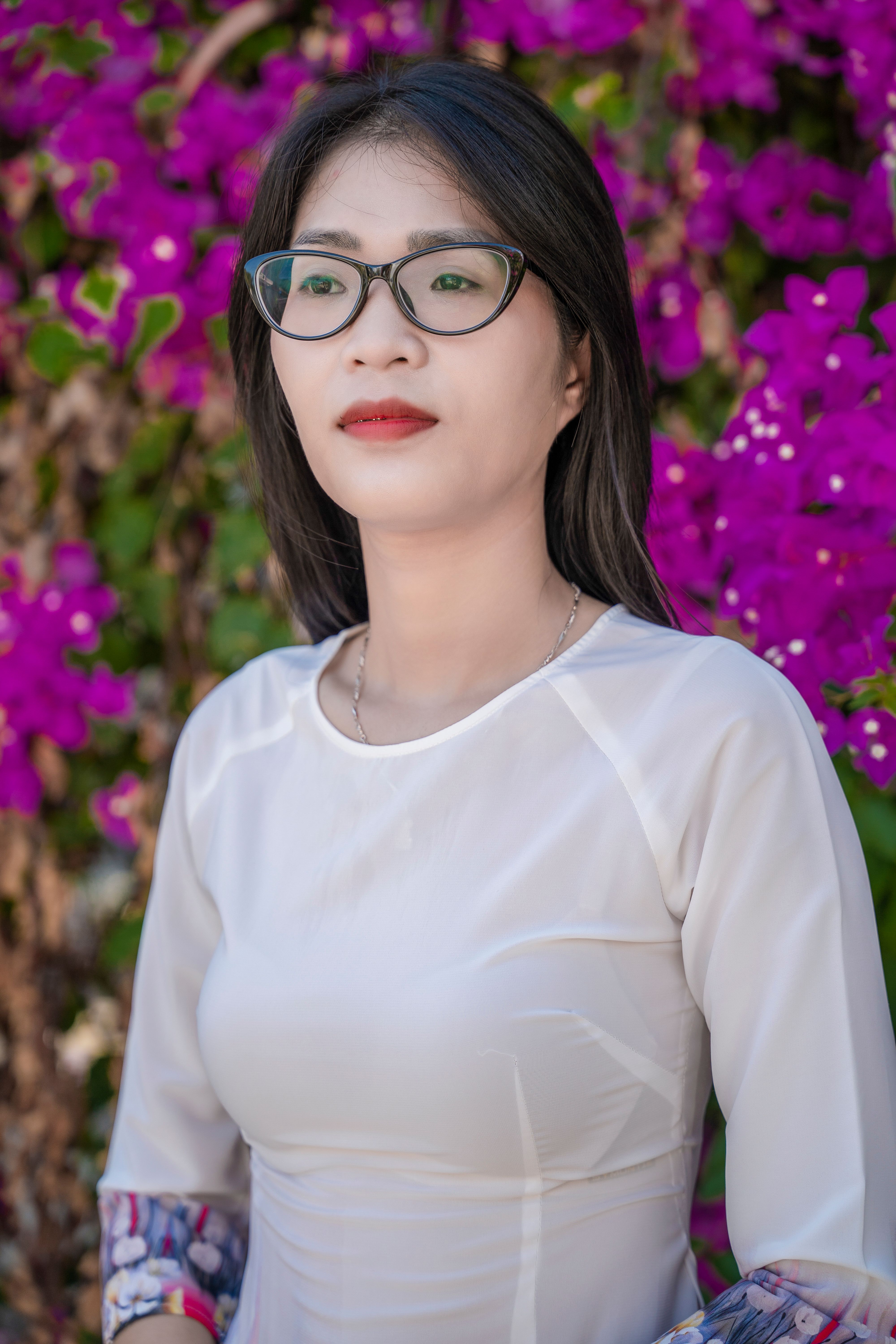 Stylish woman in glasses with vibrant bougainvillea background.