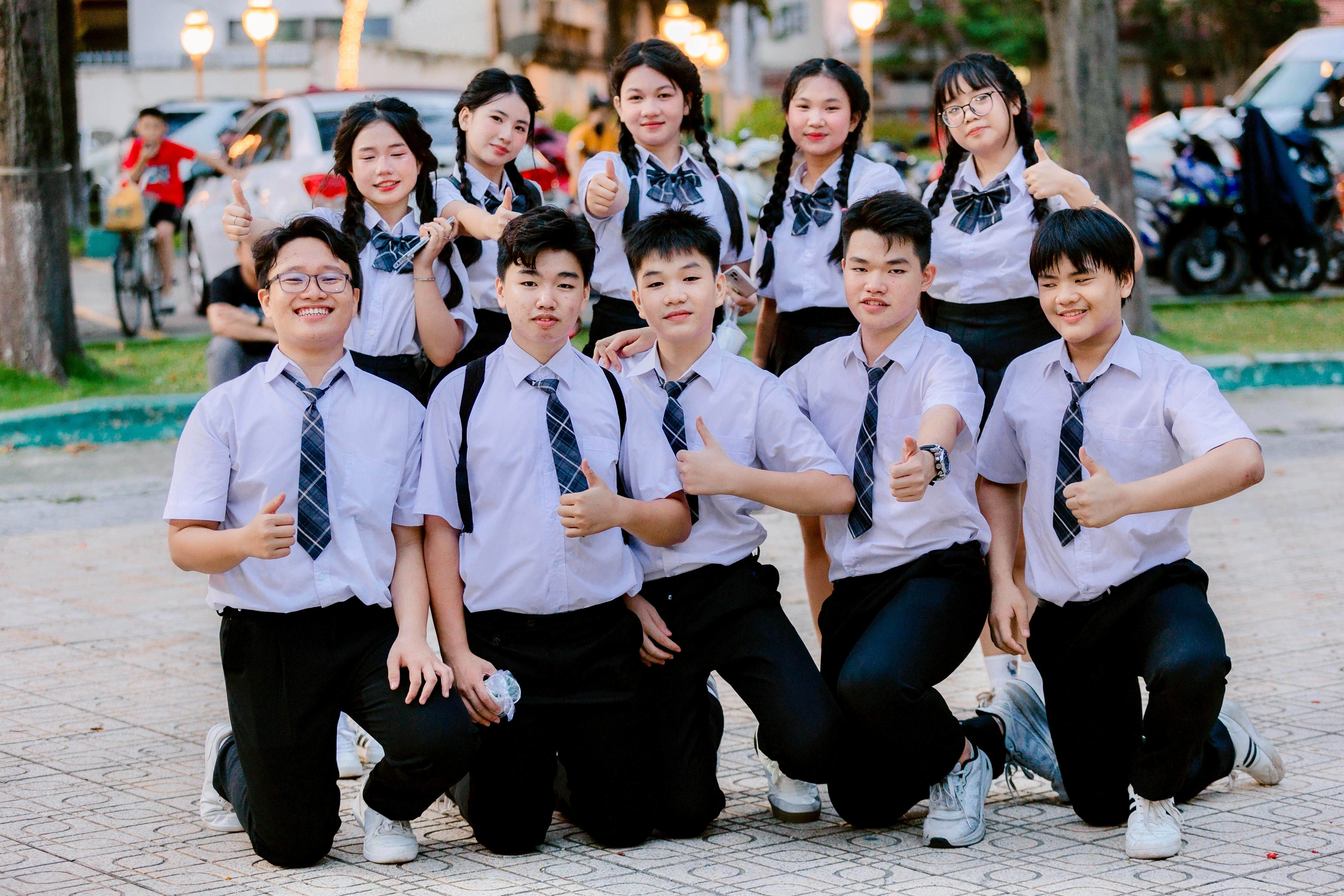 Happy group of students in school uniforms giving thumbs up outdoors.