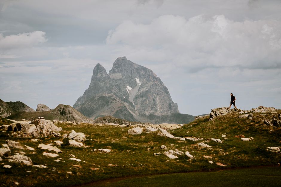 Man hiking in scenic mountain terrain with majestic Pic du Midi d'Ossau in background.