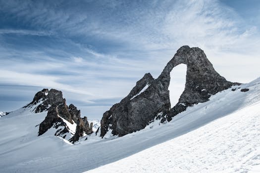 Dramatic snowy mountain landscape with a striking natural rock arch under a vivid blue sky.