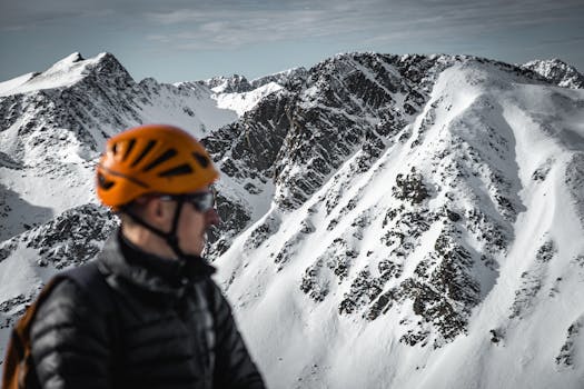 A man wearing an orange helmet gazes at a scenic snow-covered mountain range, embodying adventure and exploration.